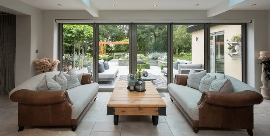Grey Origin OB-72 aluminium bifold doors open across the back of a living room onto a paved garden terrace