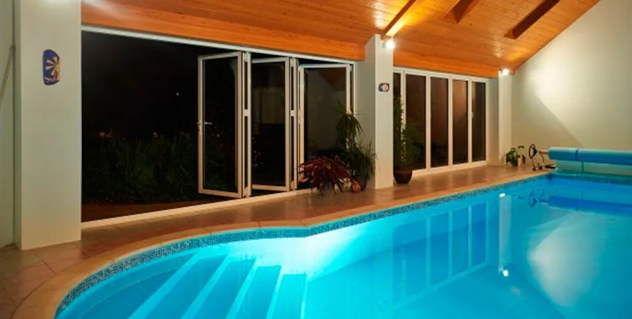 Cortizo aluminium bi-fold door beside a swimming pool at night