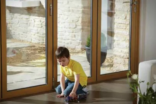 Child playing on the floor beside wood-effect aluminium bifold doors
