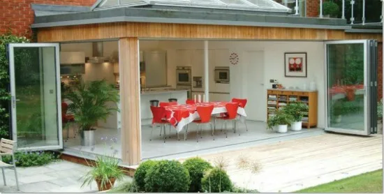 White bifold doors open across a garden room with a red dining set inside