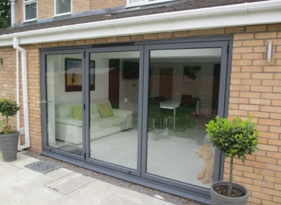 Grey aluminium bifold doors closed across a brick extension, living room visible inside