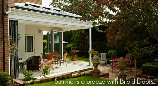 White bifold doors folded open from a garden room onto a patio