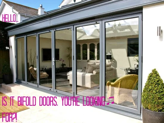 Grey bifold doors folded open along a rendered single-storey extension