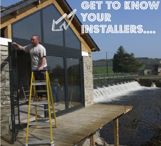 An installer on a ladder fitting glazing to a riverside stone building