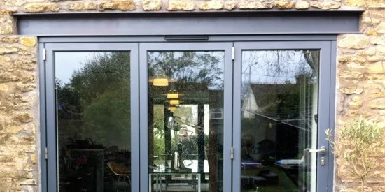 Grey bifold doors set into the stone wall of a cottage