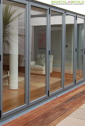 Wide grey aluminium bi-fold door, six panels, opening onto a garden